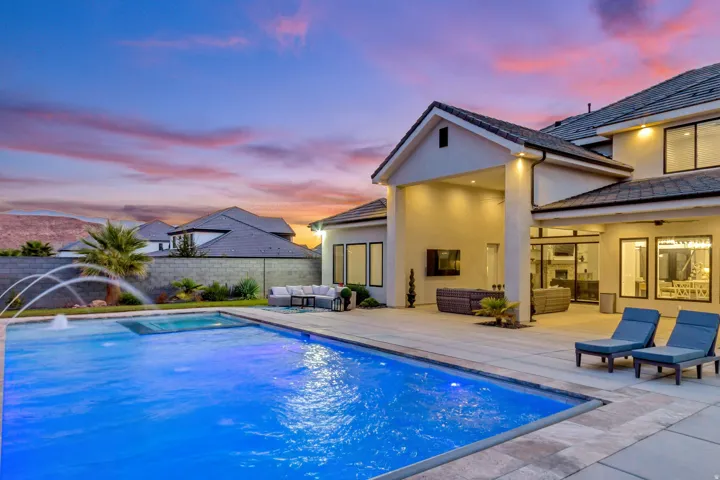 Expansive backyard featuring a rectangular swimming pool with water features, a large paved patio, and a covered outdoor living area