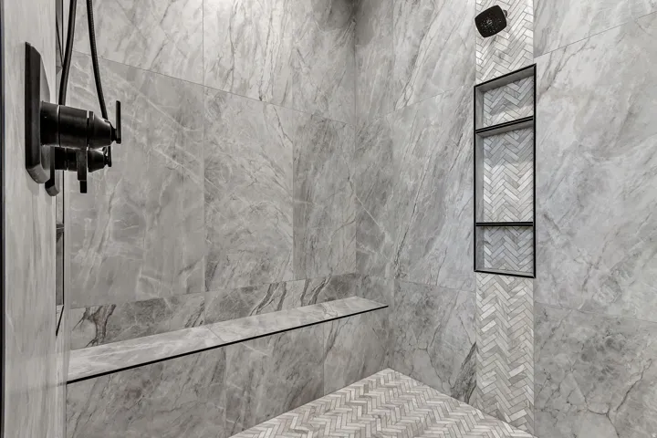 Shower featuring large format wall tiles, a built-in bench, a recessed niche with multiple shelves, a herringbone tile accent, and a matte black shower fixture