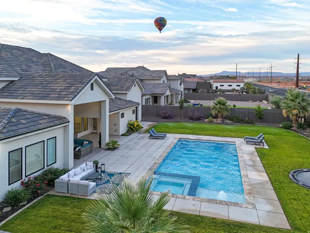 Exterior featuring a tiled roof, stucco siding, a rectangular swimming pool with integrated spa, a paved patio, and a manicured lawn