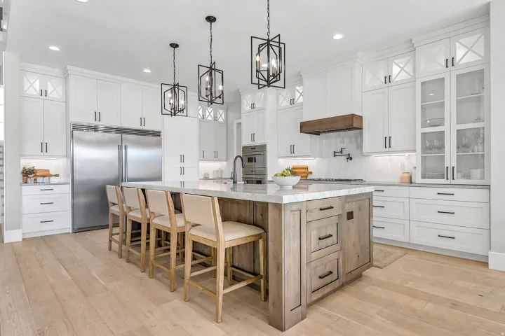 Gourmet kitchen featuring a large central island with a light-toned wood finish, white perimeter cabinetry, stainless steel appliances, and wood-finish flooring