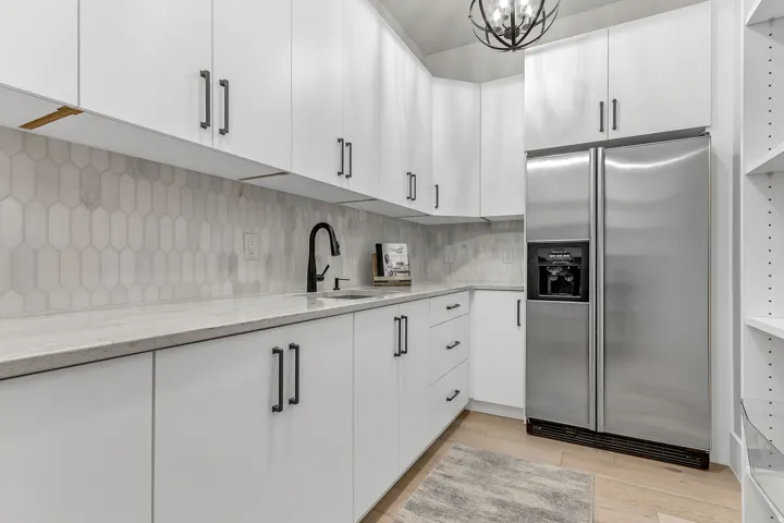 White shaker-style cabinetry, matte black fixtures, stainless steel refrigerator, light wood-finish flooring, and a decorative ceiling light fixture