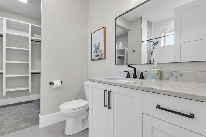White vanity with black hardware, stone-finish countertop, undermount sink, and black faucet