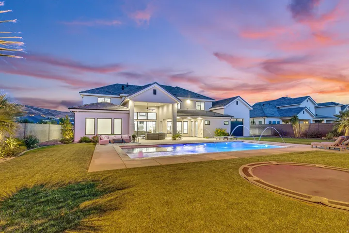 Expansive backyard featuring a manicured lawn, a rectangular swimming pool with integrated water features, and a large concrete patio