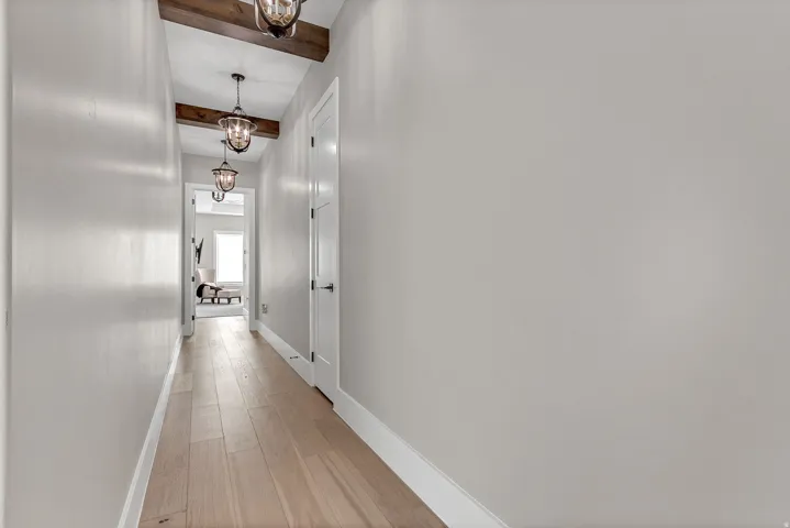 Hallway featuring wood-finish flooring, exposed ceiling beams, and pendant light fixtures