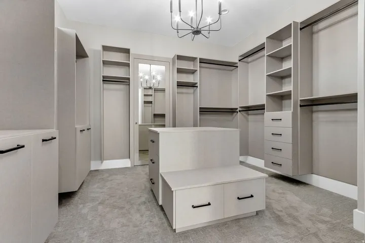 Expansive walk-in closet featuring built-in shelving, multiple hanging rods, integrated drawer storage, a central island with additional storage, and a modern chandelier