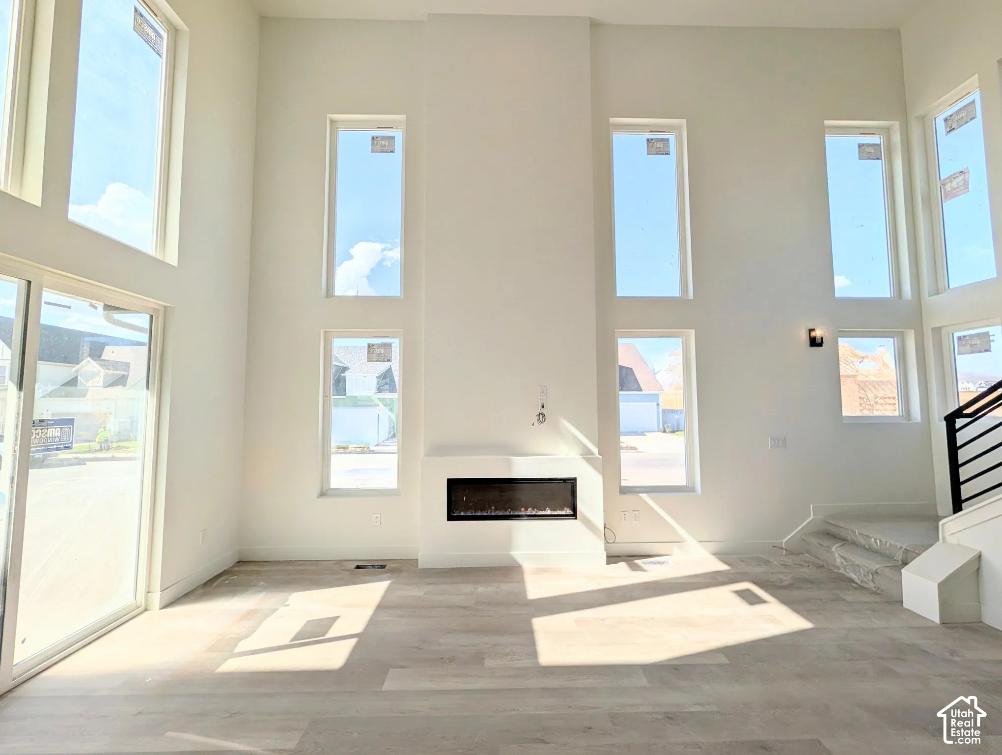 Two-story great room with a linear electric fireplace, wood-finish flooring, multiple tall windows, and a sliding glass door