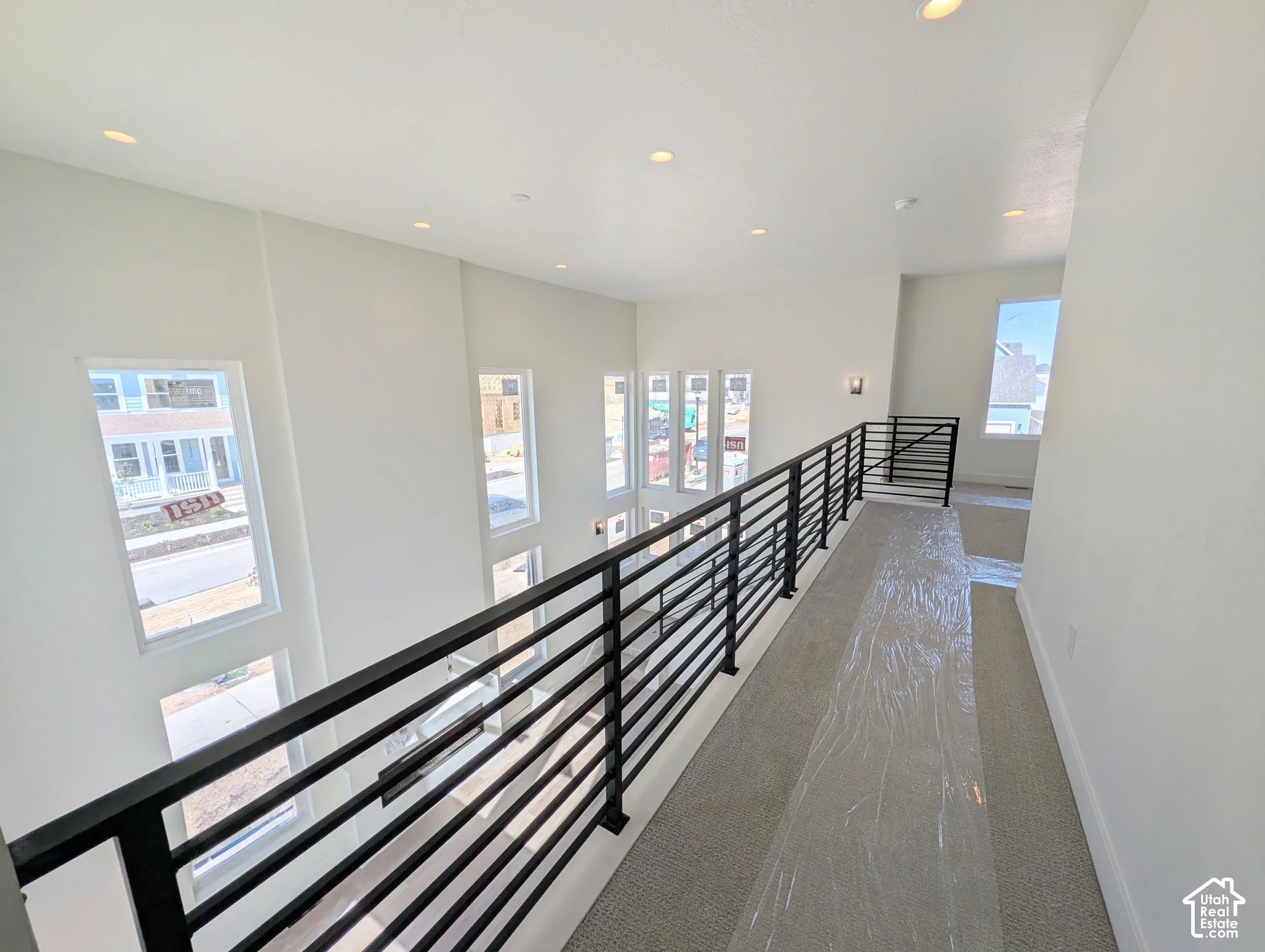 Upper-level hallway featuring a black horizontal bar railing, recessed lighting, and multiple windows