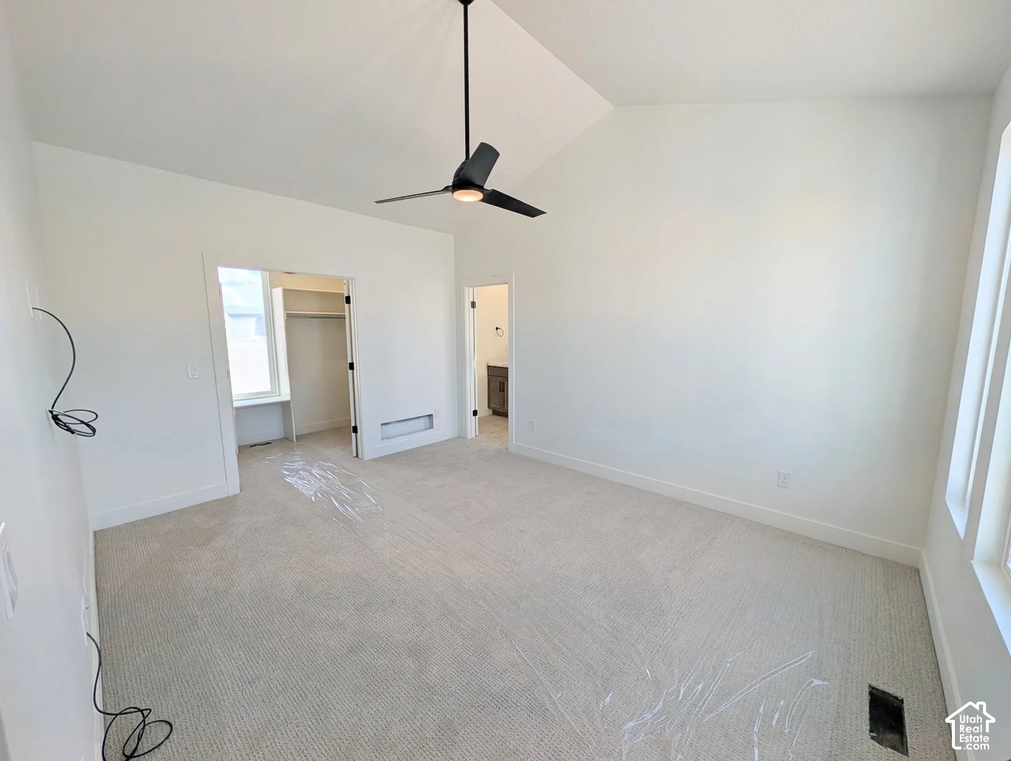 Vaulted ceiling, ceiling fan with integrated lighting, neutral carpet flooring, multiple windows, and a walk-in closet