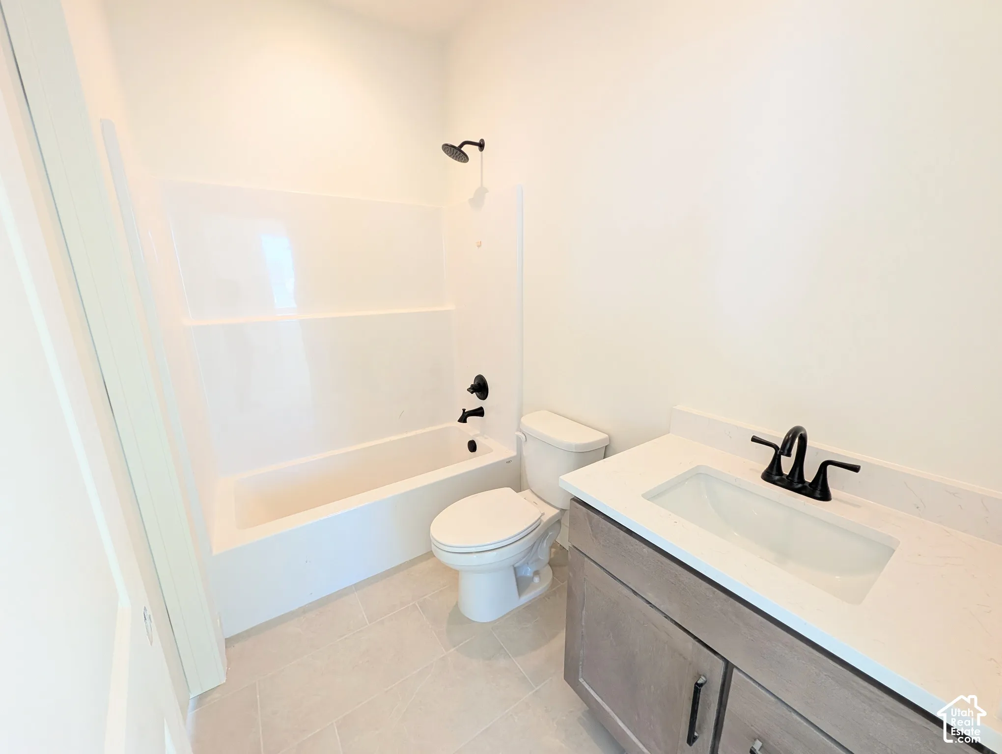 White tub and shower combination with matte black fixtures, an integrated sink vanity with a light wood-finish cabinet, and light gray tile flooring