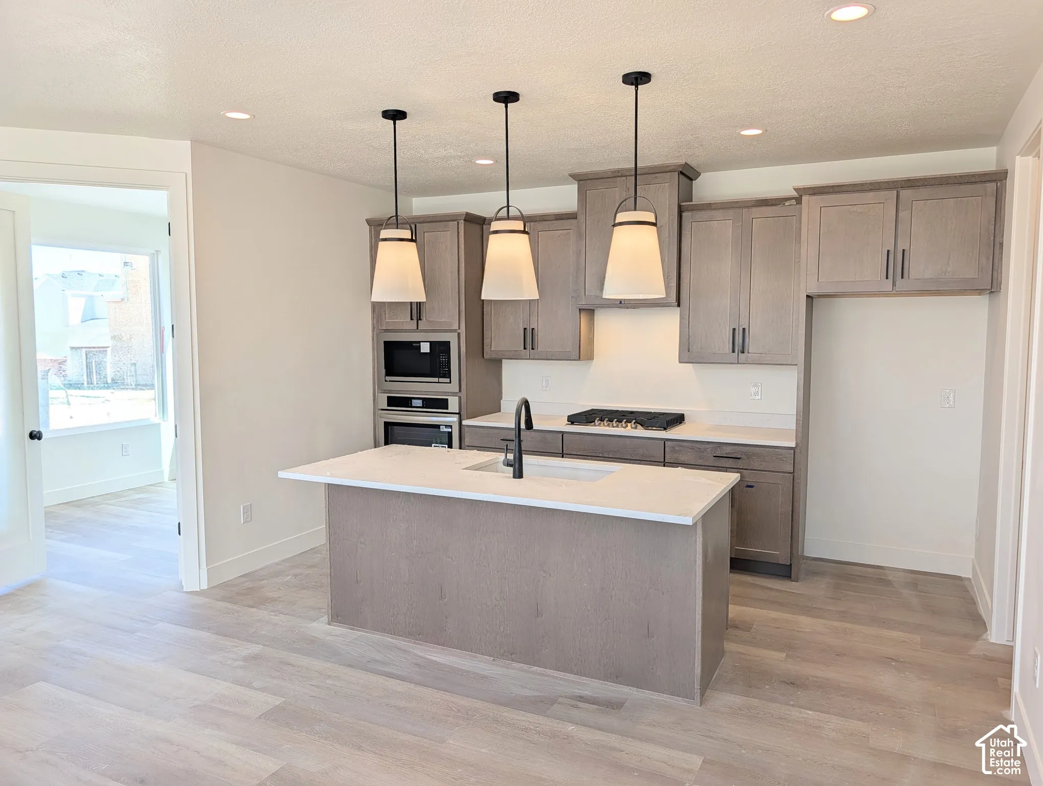 Kitchen featuring wood-finish flooring, an island with countertop, pendant lighting, recessed lighting, and built-in appliances
