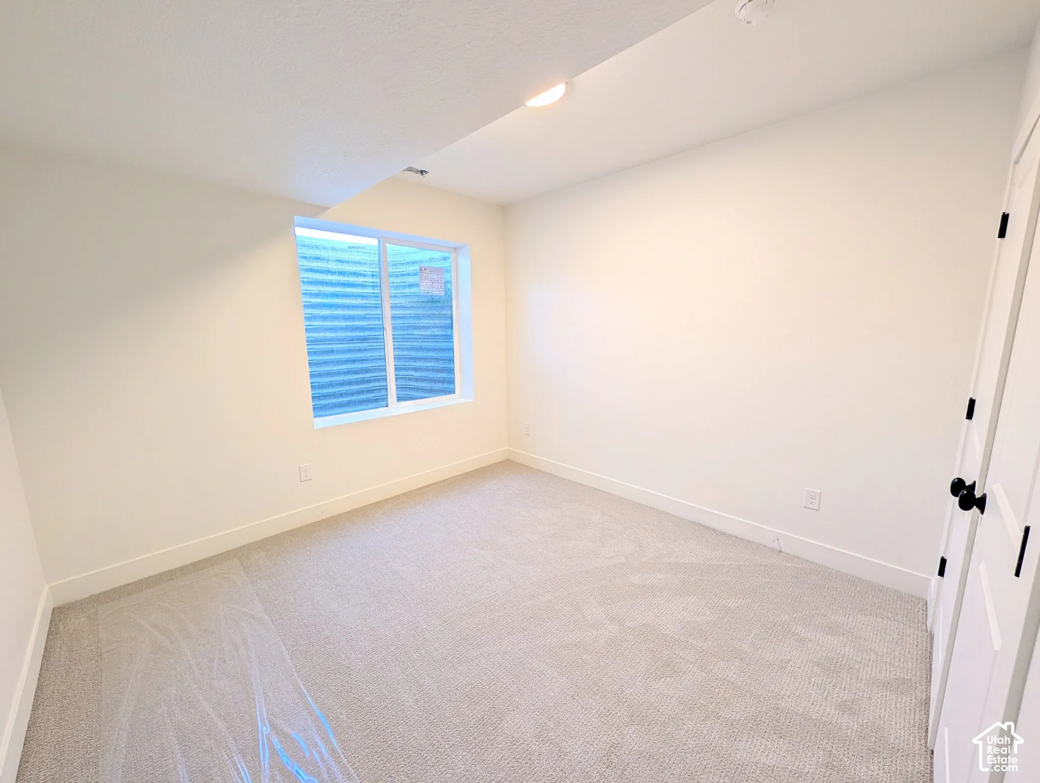 Recessed window with white trim, light-colored carpeting, white walls, white baseboards, and a white door with black hardware