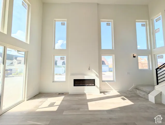 Two-story great room with a linear electric fireplace, wood-finish flooring, multiple tall windows, and a sliding glass door