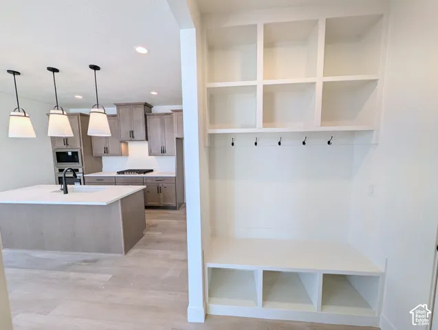 Built-in storage bench with cubbies and upper shelving, complemented by a kitchen featuring an island with a sink and pendant lighting, wood-finish flooring, and cabinetry with integrated appliances