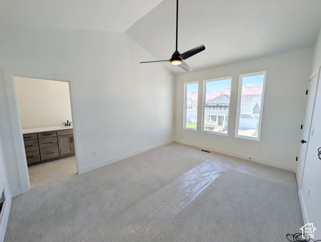 Vaulted ceiling with a contemporary ceiling fan, three large windows, light gray carpet, and white walls