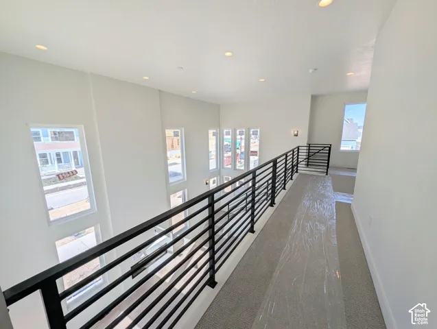 Upper-level hallway featuring a black horizontal bar railing, recessed lighting, and multiple windows