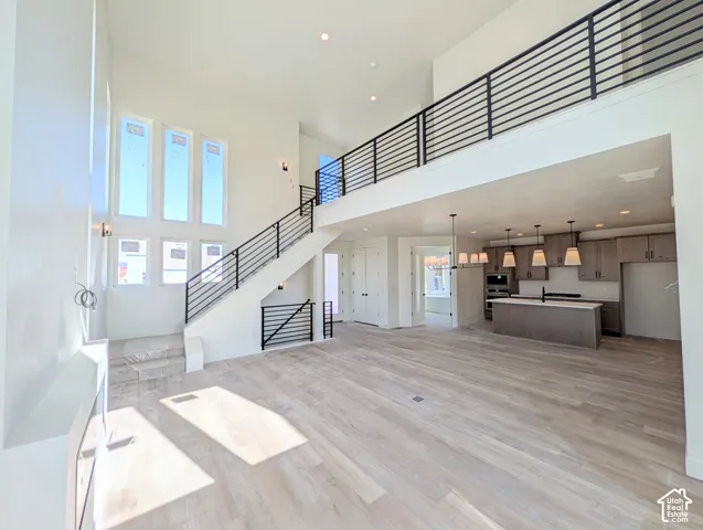 Open-concept main living area with high ceilings, large windows, wood-finish flooring, a contemporary staircase with horizontal metal railings, and a kitchen featuring an island with pendant lighting