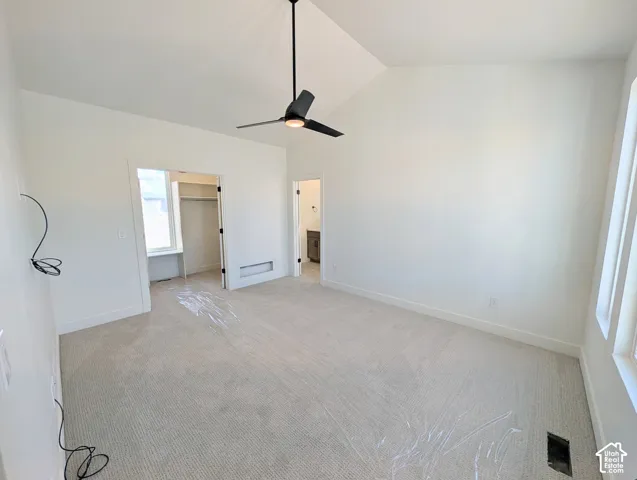 Vaulted ceiling, ceiling fan with integrated lighting, neutral carpet flooring, multiple windows, and a walk-in closet