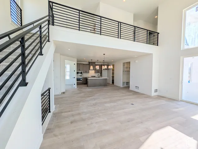 Open-concept living area with wood-finish flooring, a two-story ceiling, and a modern kitchen featuring an island and pendant lighting