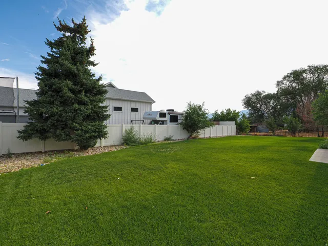 Expansive lawn area with a white privacy fence and established trees