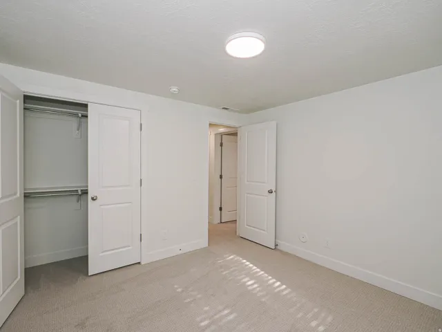 Neutral-toned wall-to-wall carpeting, white interior walls, white trim, recessed ceiling light fixture, and white bi-fold closet doors