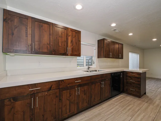 Kitchen featuring dark wood cabinetry, light-toned countertops, a stainless steel sink with a gooseneck faucet, a built-in dishwasher, and recessed lighting