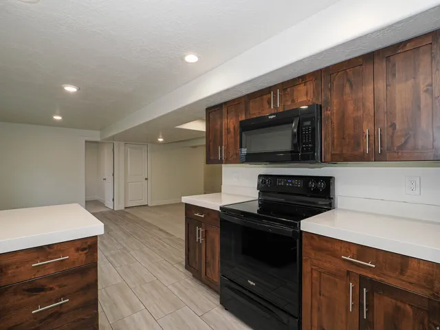 Kitchenette featuring dark wood cabinetry, light-toned countertops, and a black built-in microwave