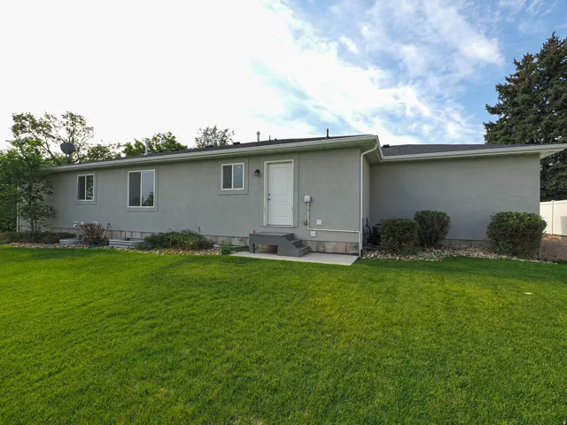 Expansive lawn with stucco exterior, multiple windows, and a rear entry door with steps