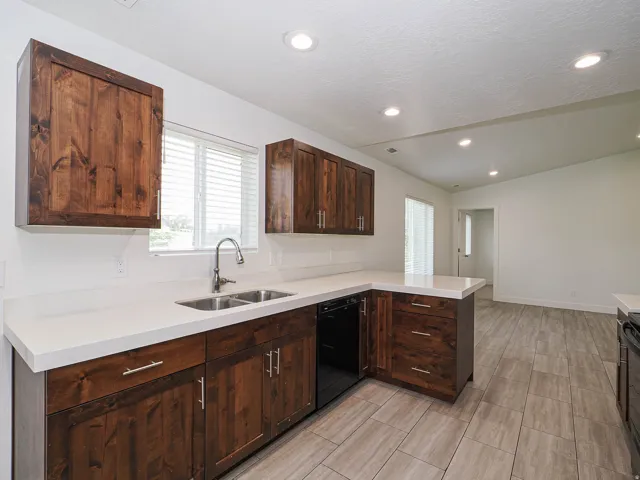 U-shaped kitchen featuring dark wood cabinetry, white countertops, stainless steel double basin sink, and recessed lighting