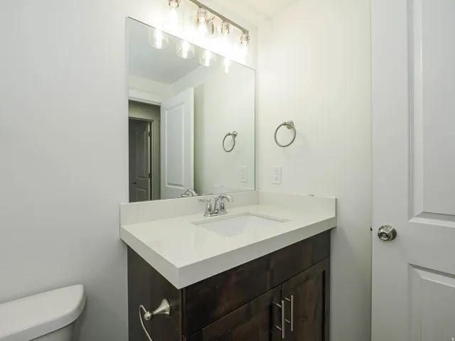 Dark wood-finish vanity with chrome hardware, white solid-surface countertop, rectangular undermount sink with chrome faucet, and rectangular mirror with five-light vanity fixture