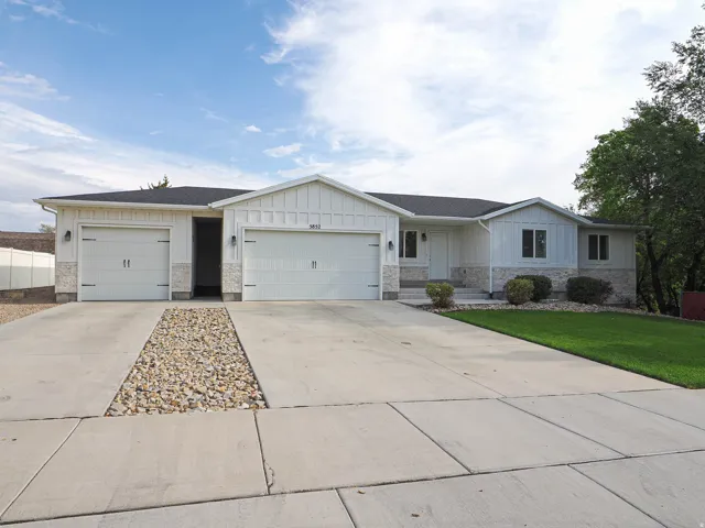 White siding exterior with a dark shingle roof, stone accenting, and two garage bays