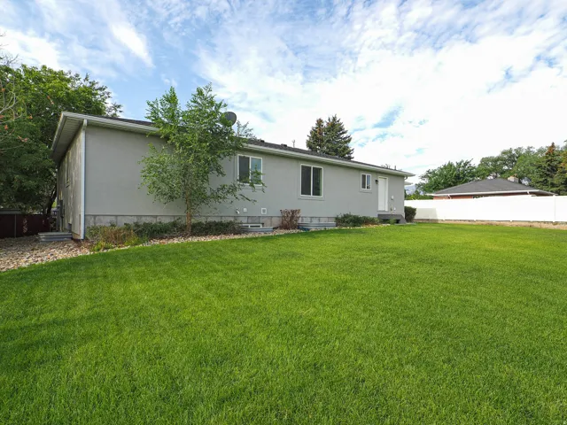 Expansive green lawn with mature trees, a stucco exterior, and a white fence