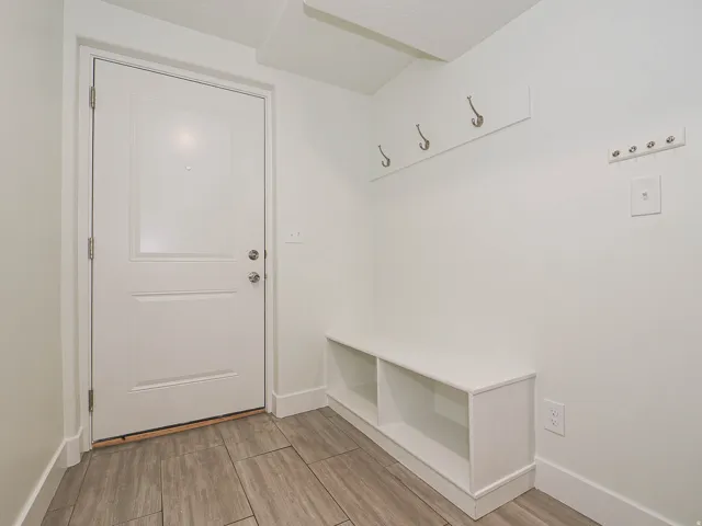 White paneled door, built-in storage bench, wall-mounted coat hooks, and wood-look tile flooring