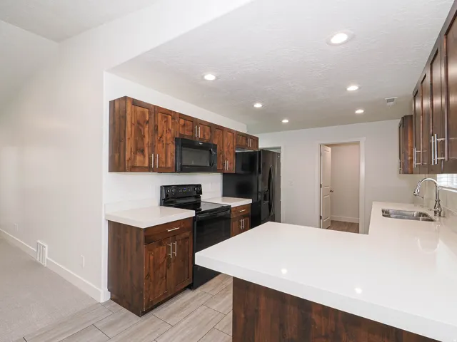 Kitchen featuring wood-finish cabinetry, white solid surface countertops, black appliances, and recessed lighting