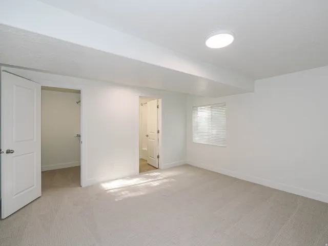 Neutral carpet flooring, white walls, and a window with blinds