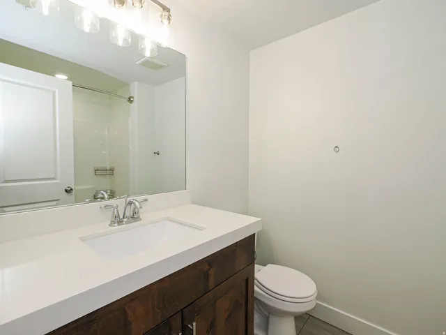 Spa-inspired bathroom featuring a wood-finish vanity with ample storage, white quartz countertop, chrome widespread faucet, and large framed mirror with integrated lighting
