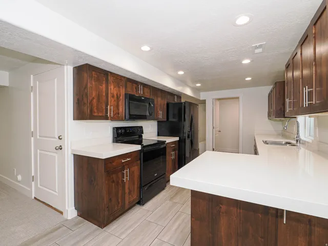 Kitchen featuring wood-finish cabinetry, white countertops, black appliances, and recessed lighting