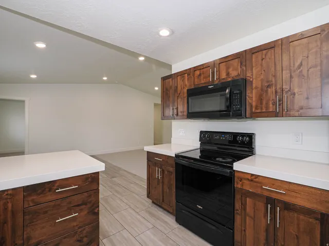 Kitchen featuring rich wood cabinetry, light countertops, black appliances, recessed lighting, and tile flooring