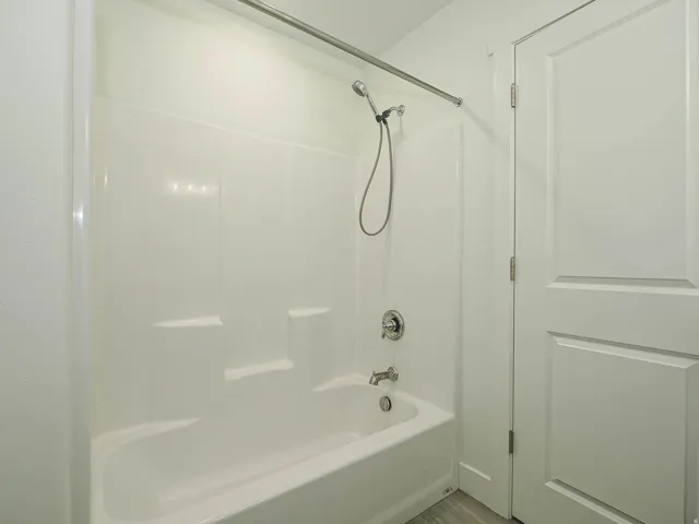 Bathtub with shower kit, chrome fixtures, and white panel door