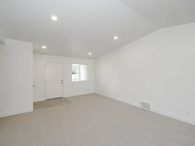 Recessed lighting, light gray carpeting, white walls, and a window with natural light