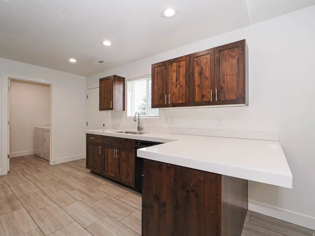 Wood-finish cabinetry, white solid-surface countertops, stainless steel sink, recessed lighting, and tile flooring