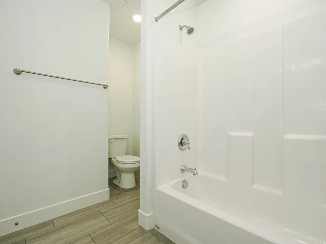 Full-sized bathtub with an integrated shower, chrome fixtures, and white tile-finish flooring