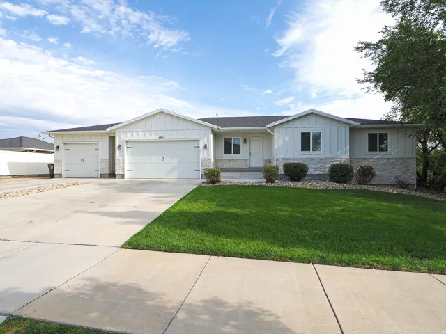 Exterior featuring white vertical siding, light-toned stone accents, a dark shingle roof, a two-car garage, and a concrete driveway