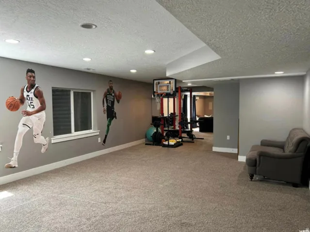 Recessed lighting illuminates a spacious carpeted area with a window, leading to a dedicated fitness zone