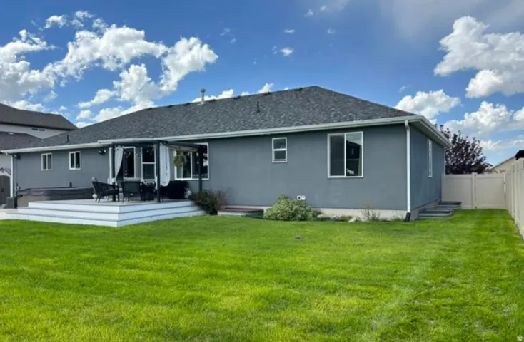 Exterior featuring a grey stucco finish, white trim, a multi-level deck, a dark-colored pergola, and a privacy fence