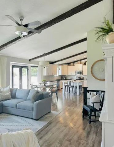 Vaulted ceiling with dark exposed beams, wood-finish flooring, and white kitchen cabinetry