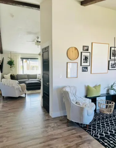 Wood-finish flooring throughout, complemented by a black interior door, and exposed ceiling beams