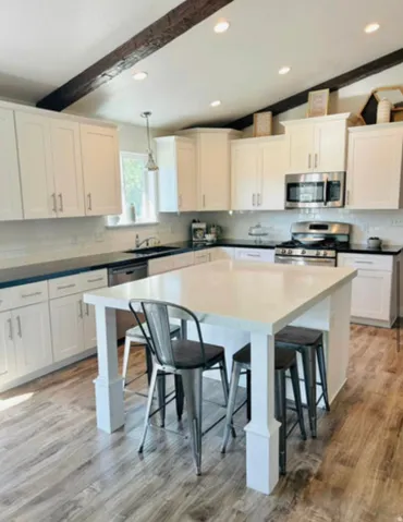 White shaker cabinetry with dark countertops, wood-finish flooring, and a central island with a light-toned countertop