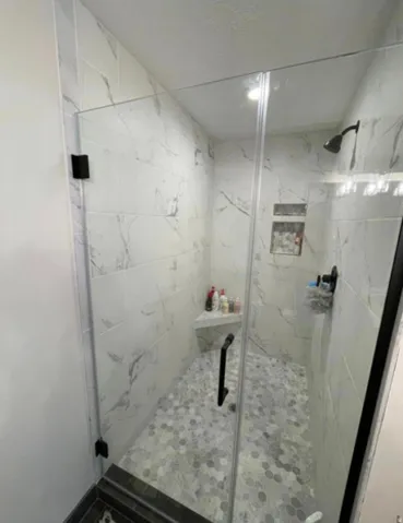 Glass-enclosed shower with white marble-look wall tiles, hexagonal floor tiles, a built-in shower bench, and a recessed niche