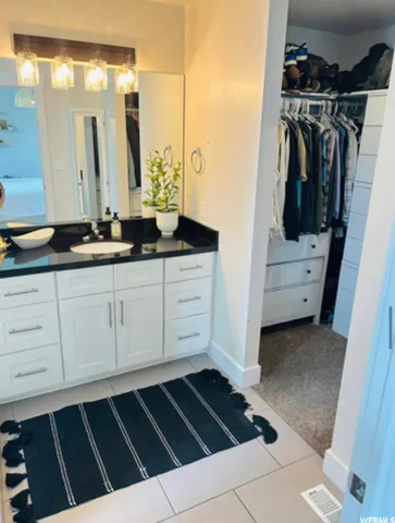 Double vanity with white cabinetry, black countertop, and vessel sink