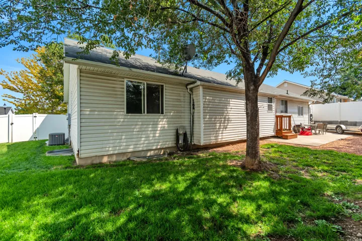 Expansive green lawn, white vinyl fencing, concrete patio, exterior siding, and a wooden deck with railing